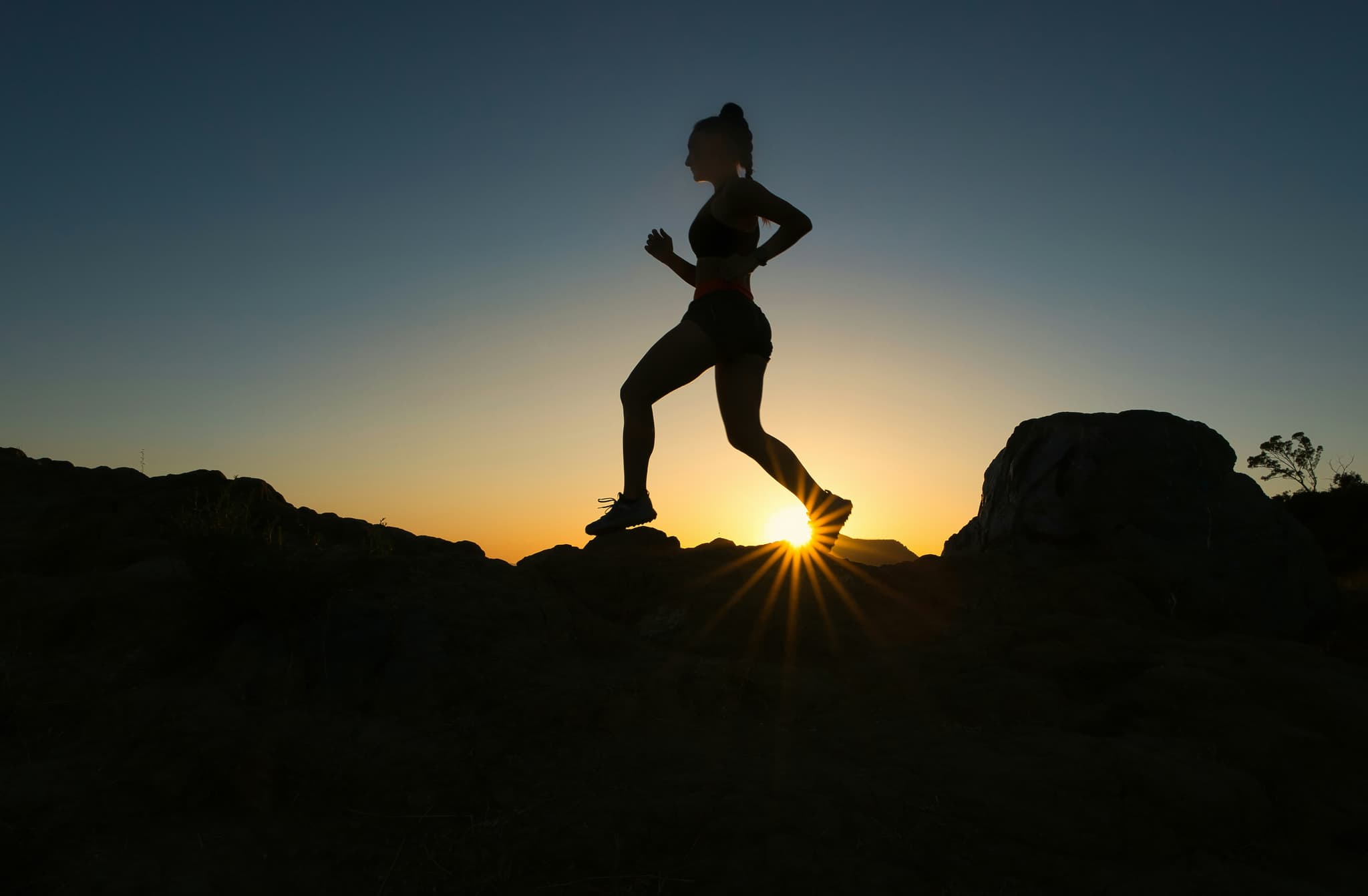 Silhouette of a woman trail running over rocks at sunset