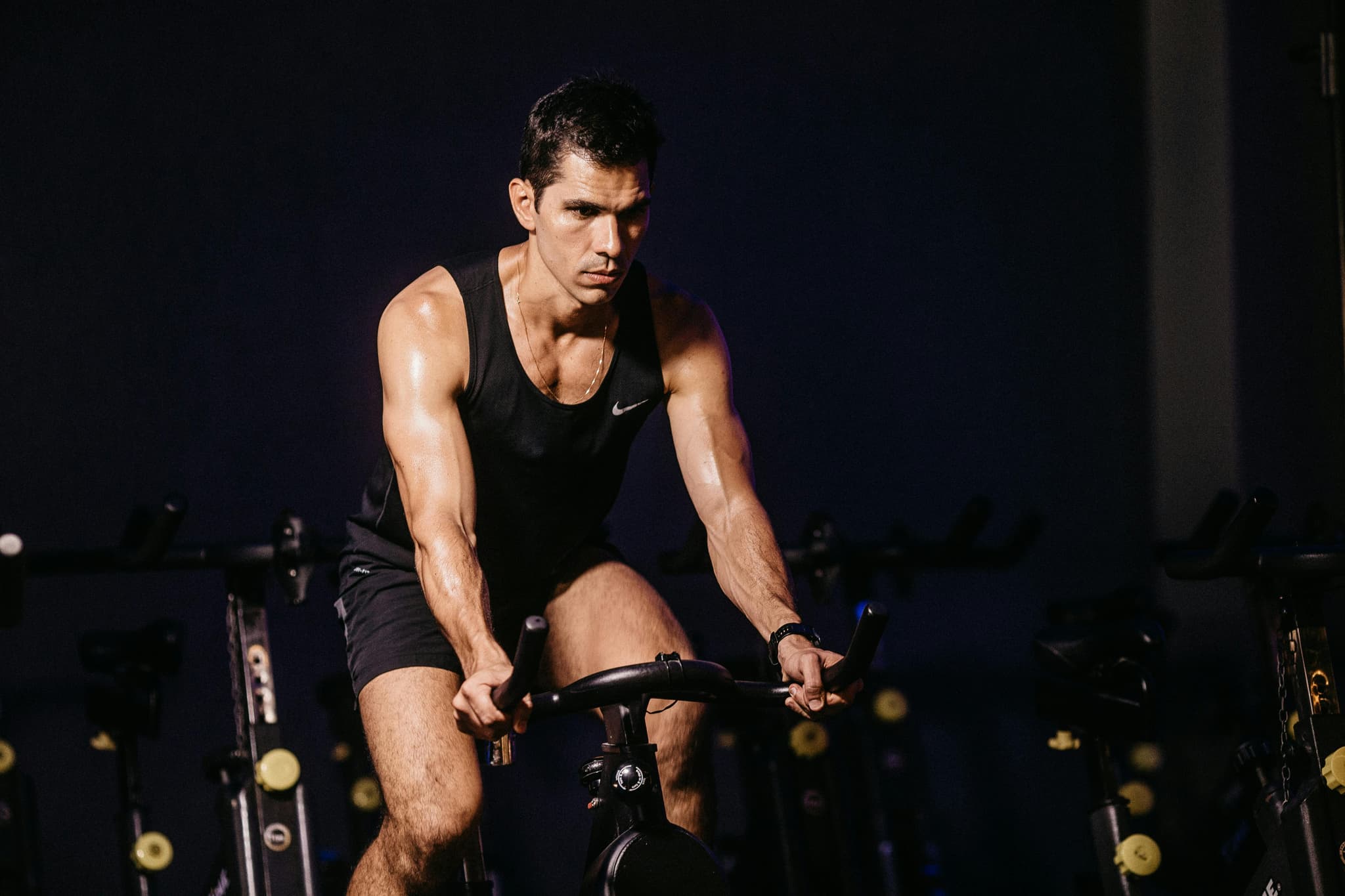 Indoor Cycling Session in Dark Studio Man riding a stationary bike during an indoor cycling class in a dark studio.