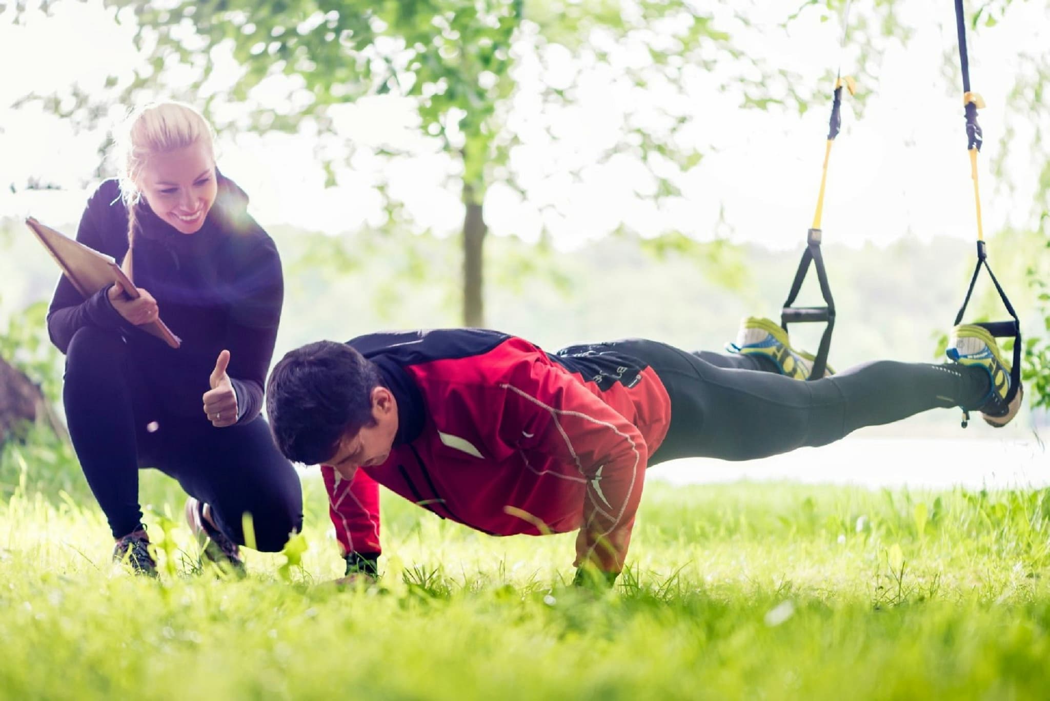 Outdoor Plank Exercise with Suspension Straps Trainer coaching a man doing a plank exercise with suspension straps outdoors.