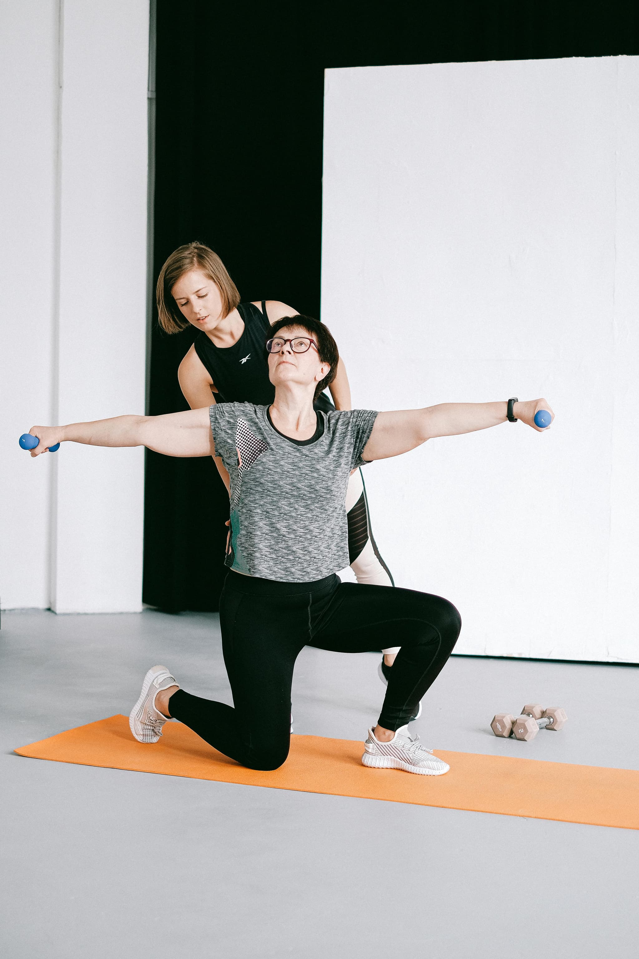 Trainer Assisting Lunge Exercise With Dumbbells Trainer assisting a woman doing a lunge with dumbbells on a yoga mat.